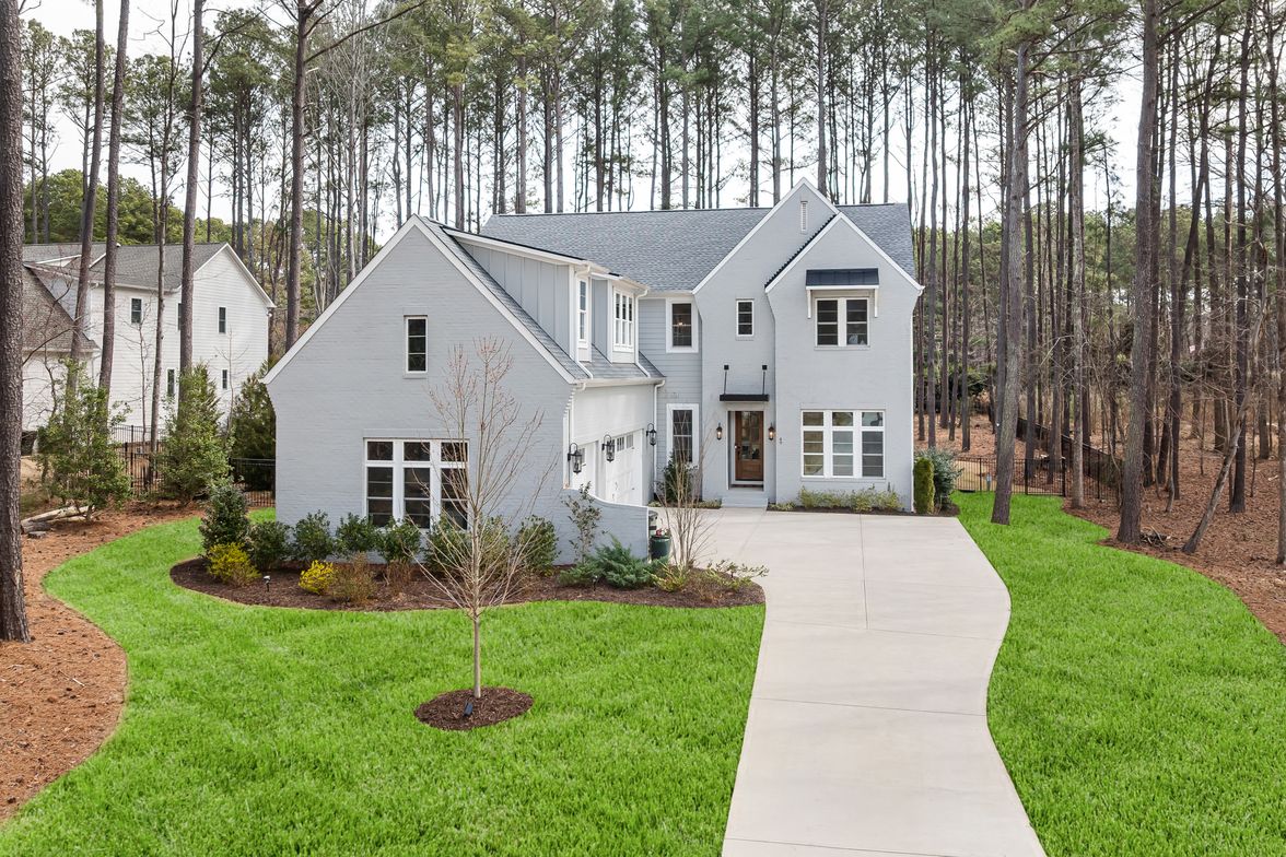 Two-story house ringed closely by tall mature pines that rise well above the roofline.